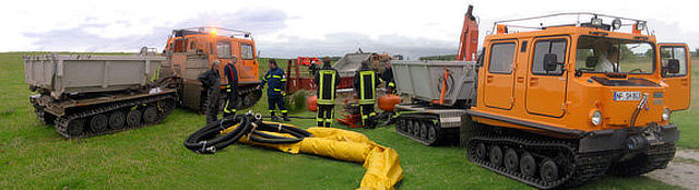 Zwei Kettenfahrzeuge, dazwischen Einsatzkräfte und eine gelbe Ölsperre.